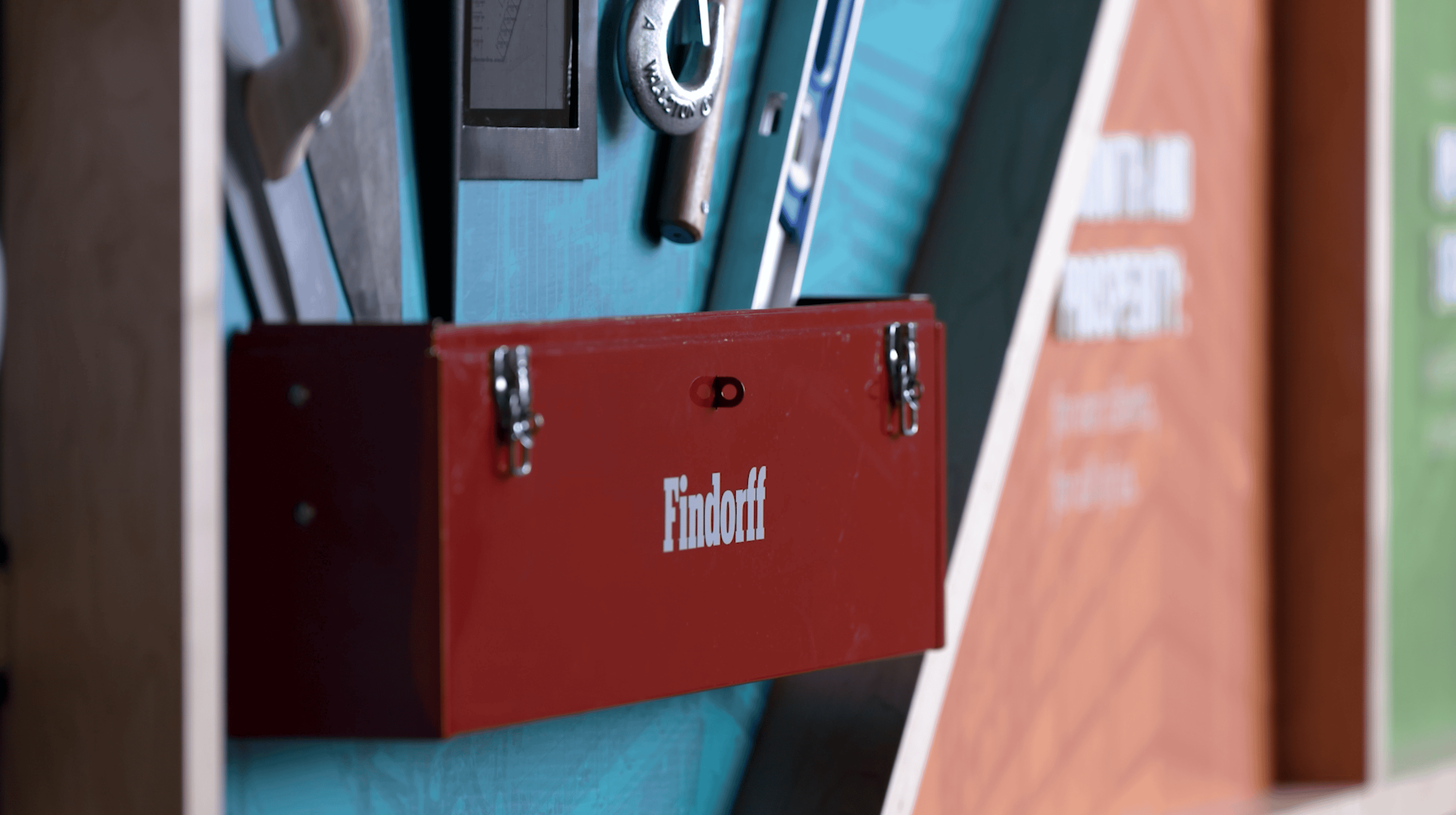 Display of construction tools and equipment in a branded Findorff toolbox setup by Thysse. The installation features a trowel, wrench, hammer, and level, mounted against a blueprint-themed backdrop as part of the facility branding project.